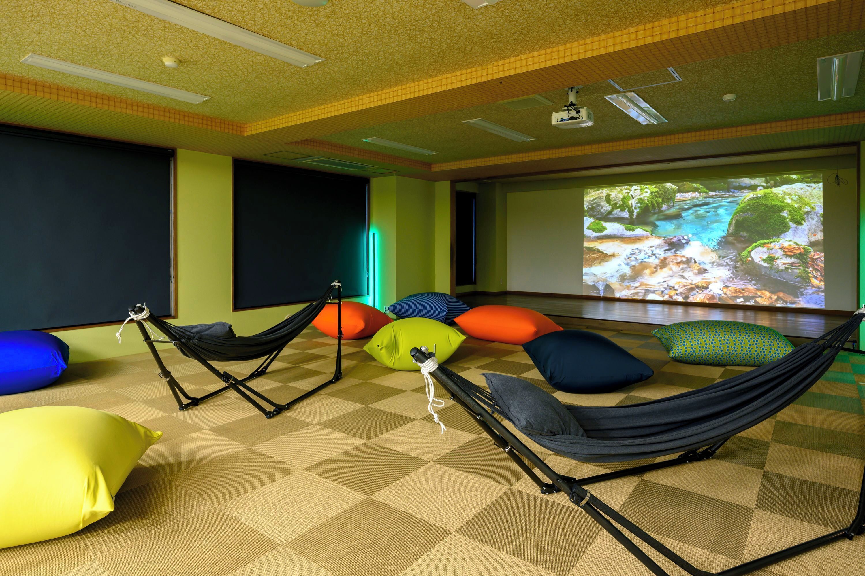A room with a large screen displaying a nature scene, a hammock, and colorful cushions on a checkered floor.