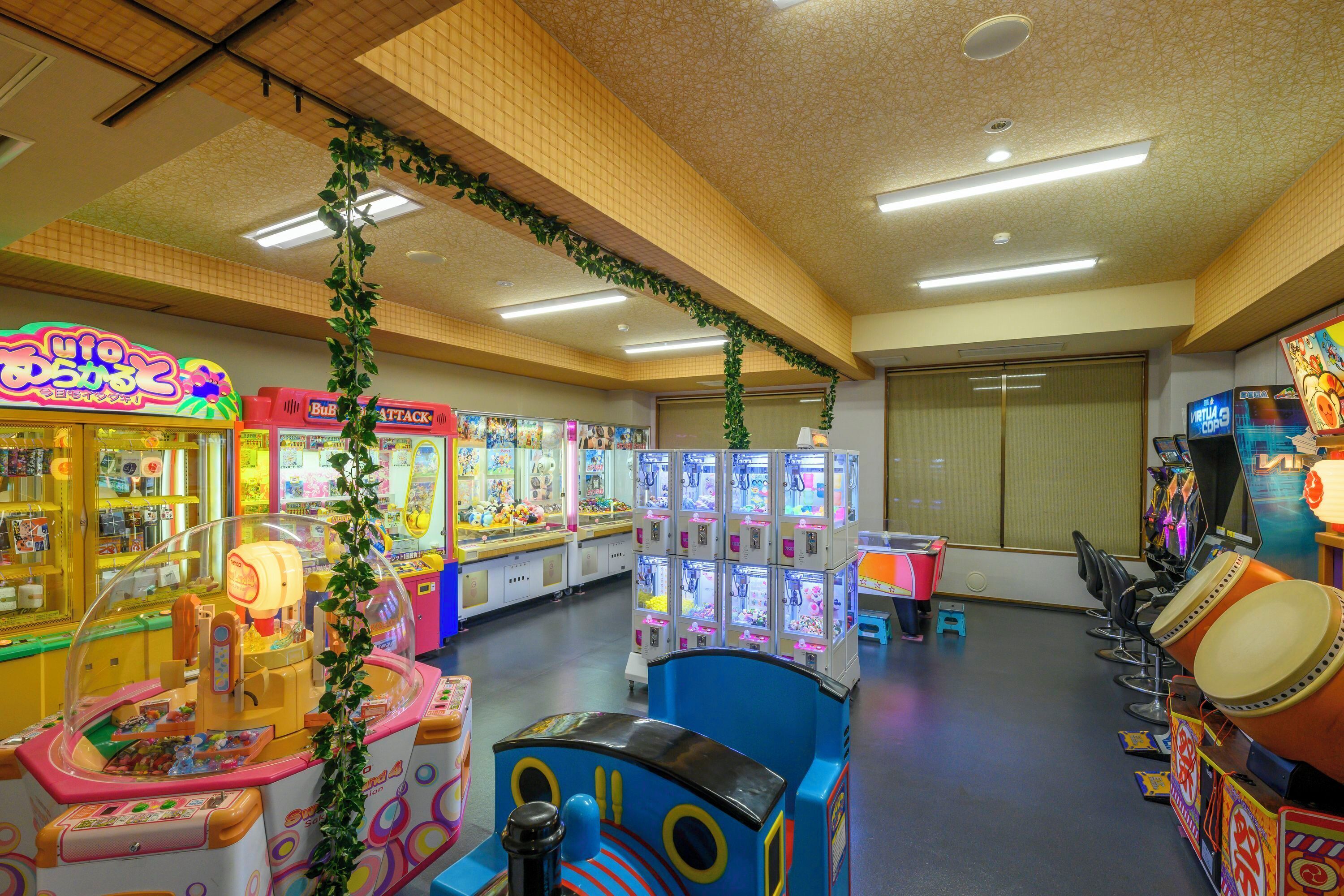 A brightly lit arcade with various gaming machines, including claw games and racing games.