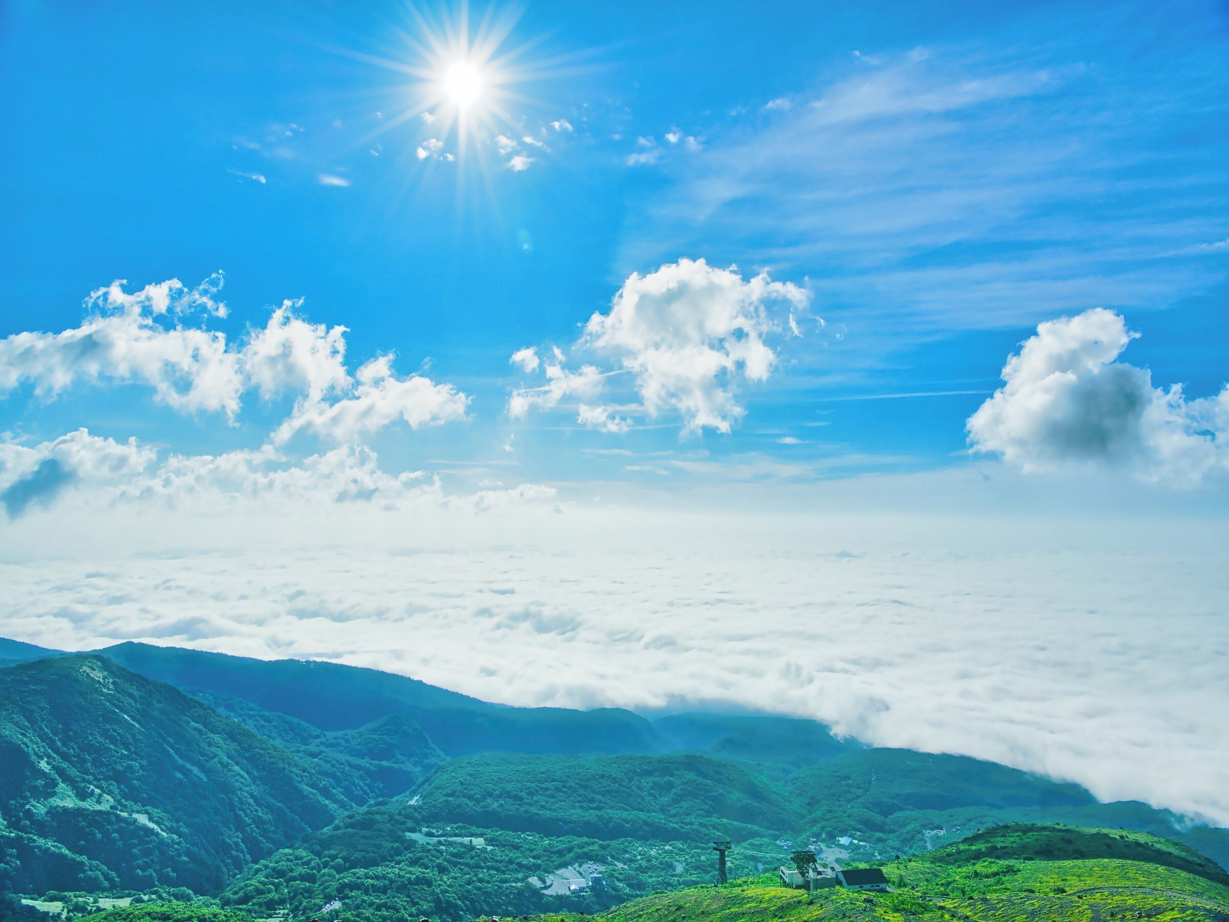 A mountainous landscape with a clear sky, a sun shining, and a village nestled among the hills.