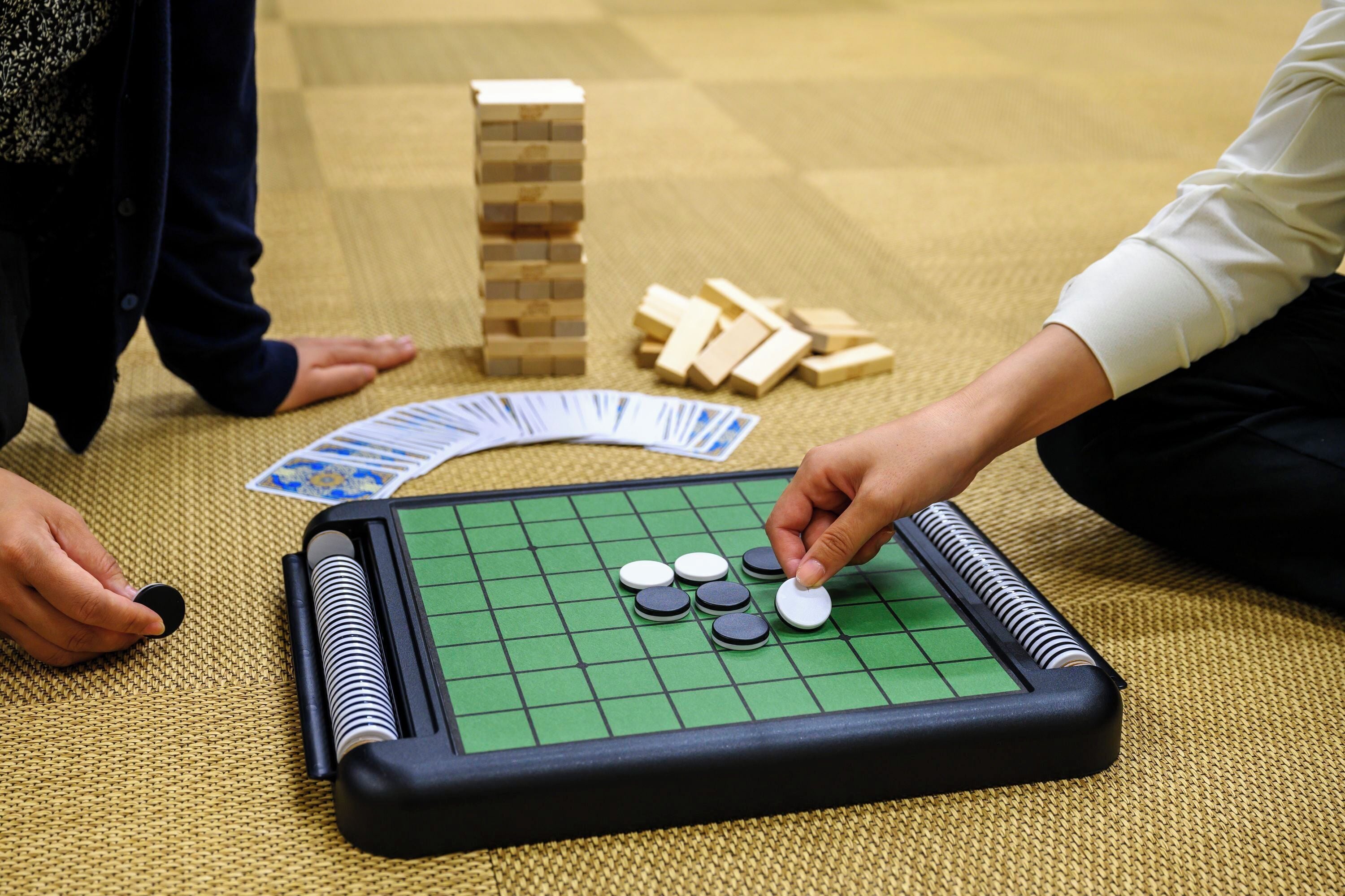 Un jeu de Go, avec un plateau à carreaux verts, des pierres noires et blanches, et des blocs de bois, le tout disposé sur un tapis tissé.