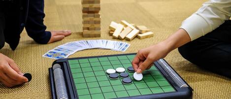 Un jeu de Go, avec un plateau à carreaux verts, des pierres noires et blanches, et des blocs de bois, le tout disposé sur un tapis tissé.