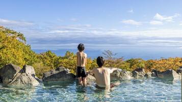 Two people standing in a clear pool surrounded by rocks and trees.