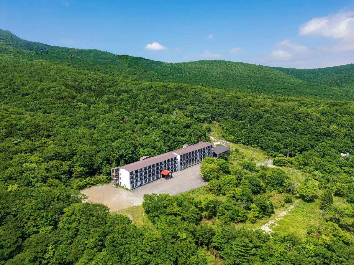 A building with a long, rectangular structure and a covered outdoor area, surrounded by dense green forest.