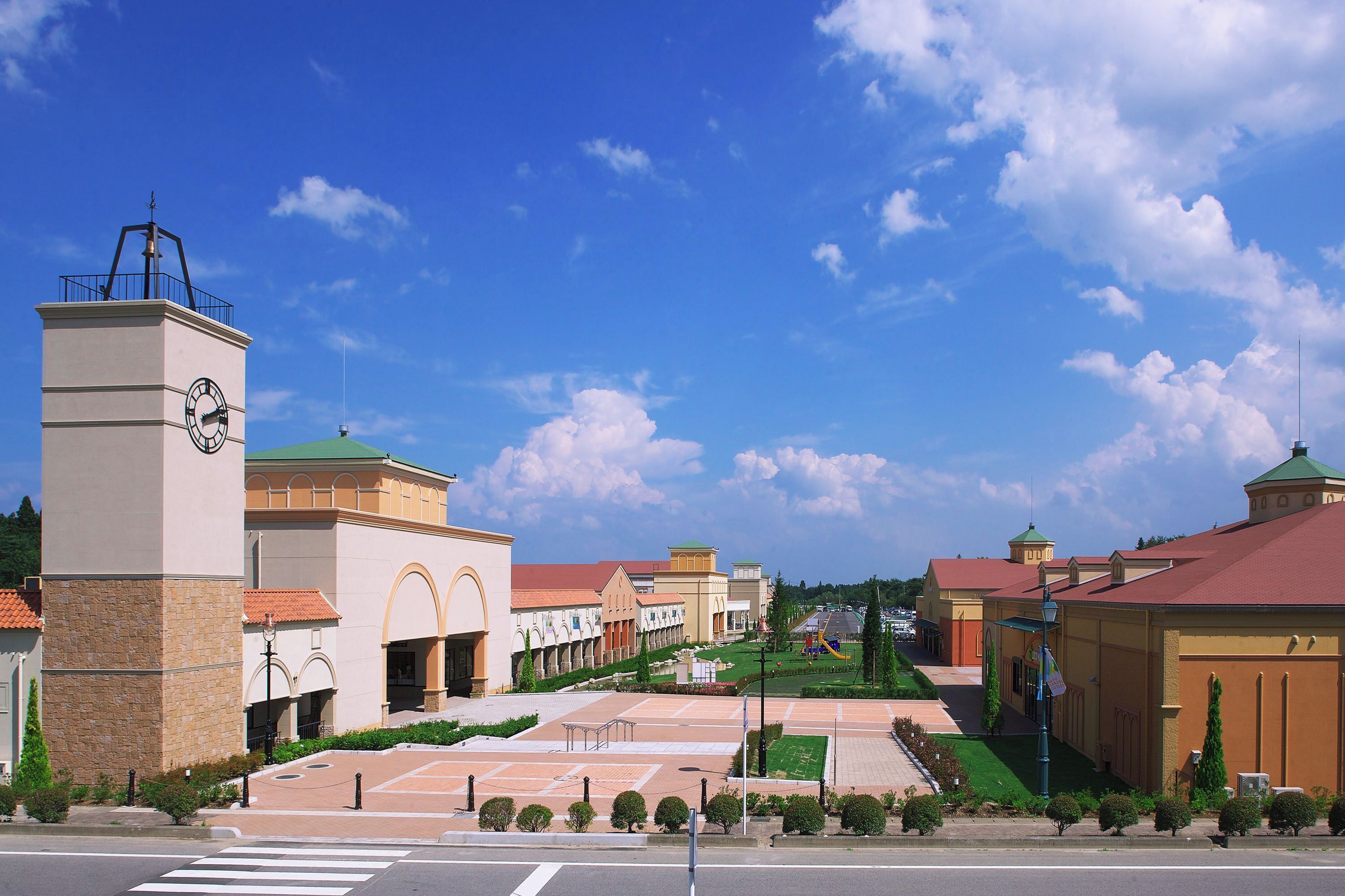 A building with a clock tower, a green roof, and a paved courtyard with benches.
