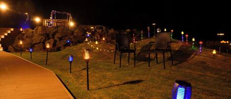 A nighttime outdoor area with a wooden deck, seating, and decorative lights.
