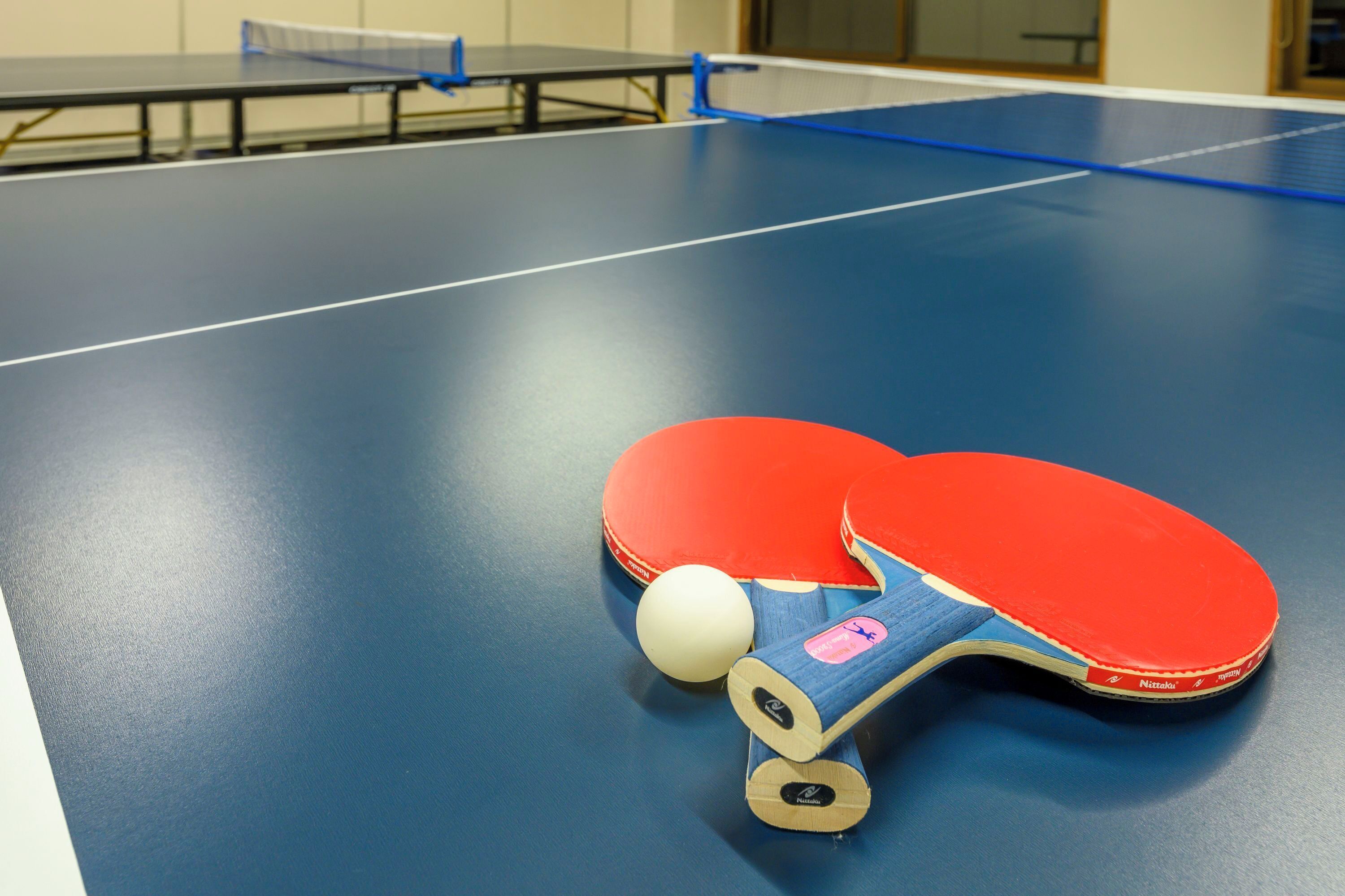 Une table de ping-pong avec un plateau bleu, une raquette de ping-pong rouge et une balle.