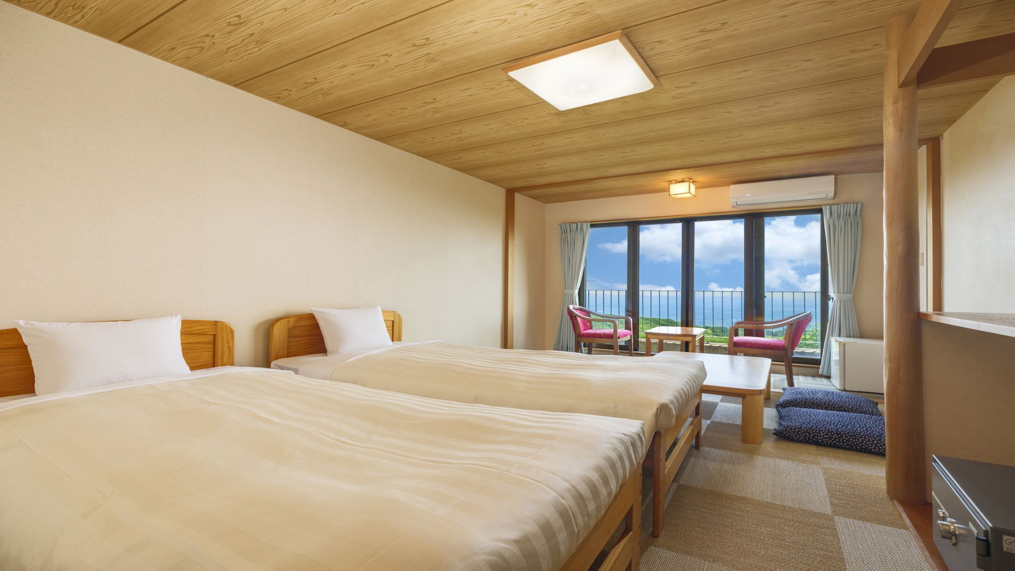 A hotel room with two beds, a balcony with chairs, and a view of the sea.