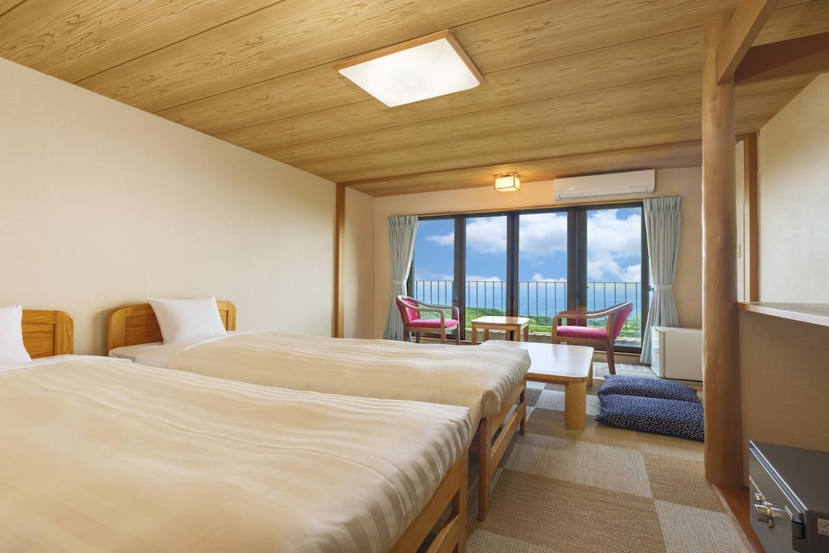Habitación de hotel con dos camas, un balcón con sillas y vista al mar.