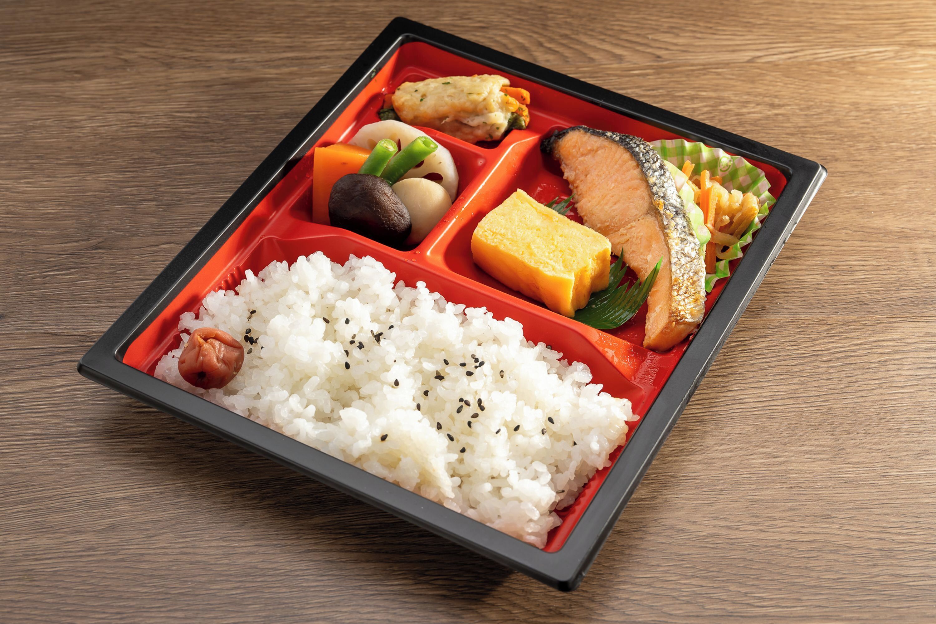 Een bento box met rijst, vis, tofu en groenten op een houten tafel.