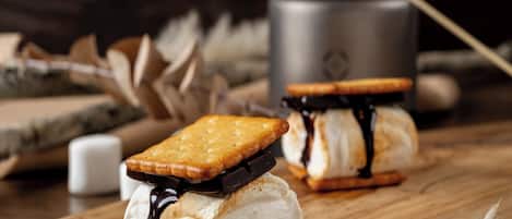 Dos sándwiches de helado con salsa de chocolate y malvaviscos sobre una superficie de madera.