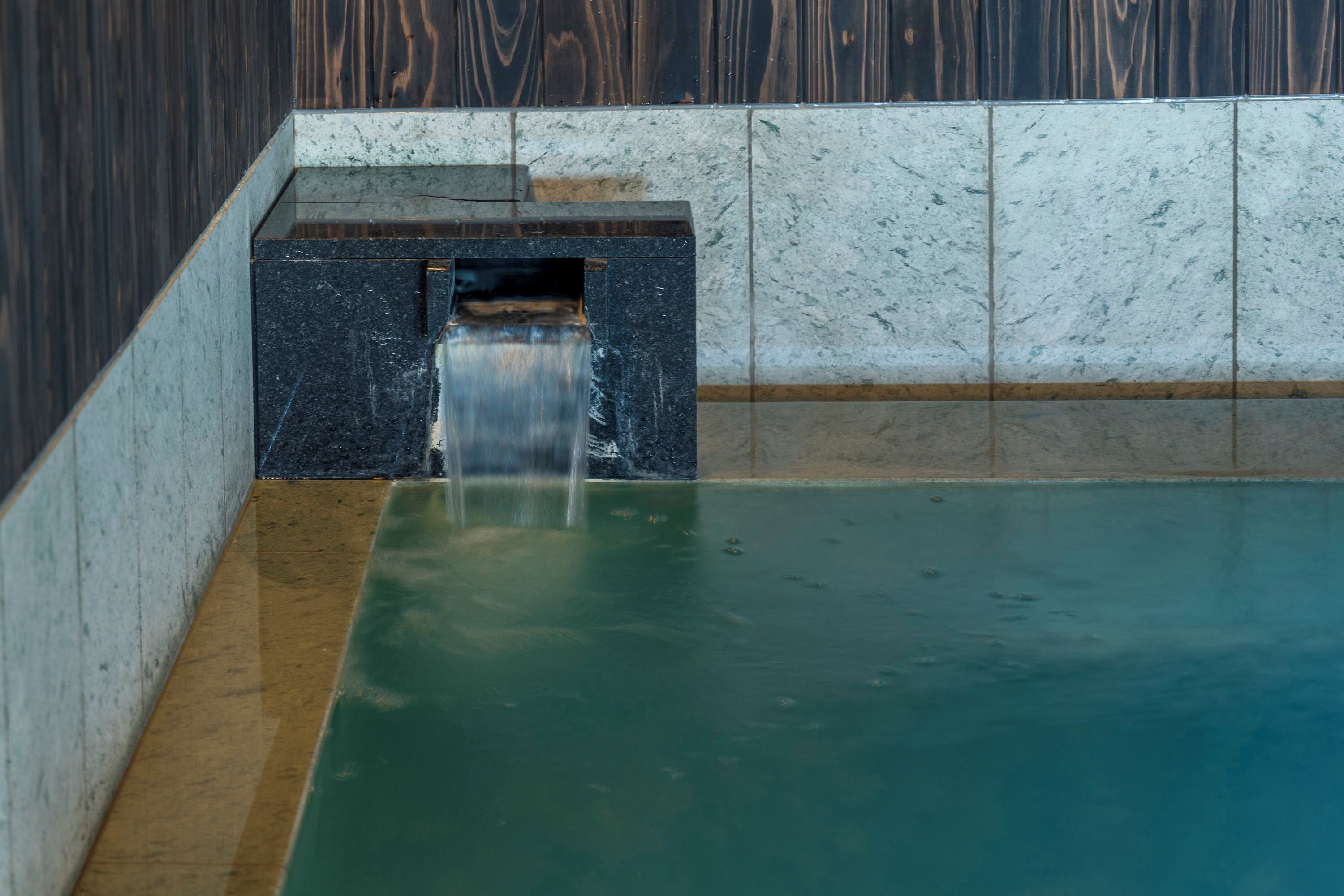 Una piccola piscina interna con una cascata, circondata da pareti piastrellate.