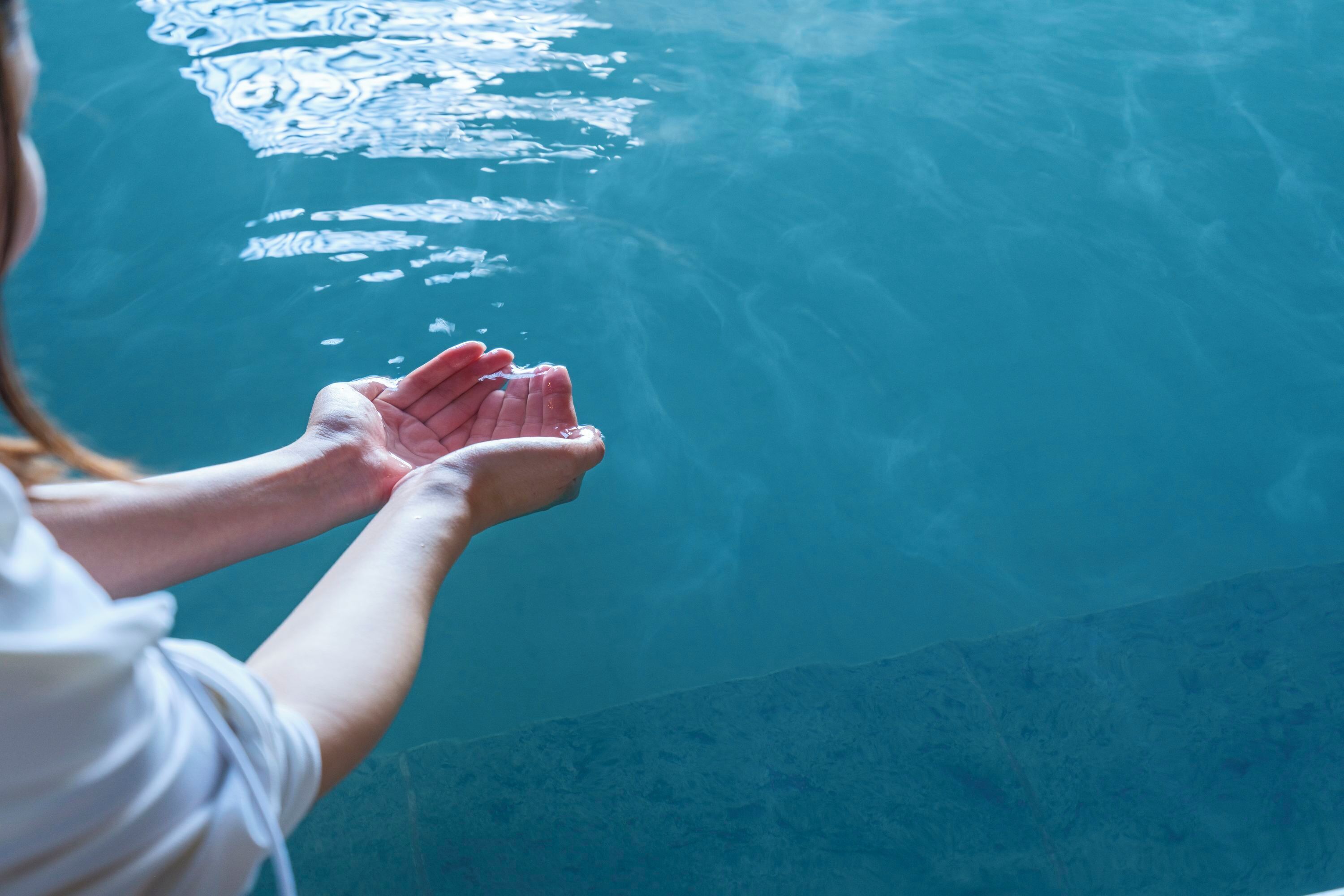 A person holding a clear glass of water over a pool.