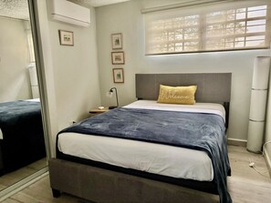 Ein Schlafzimmer mit Bett, Nachttisch, Lampe und einem Fenster mit Jalousien.