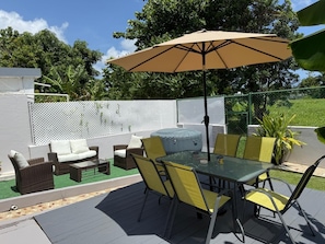 Eine Terrassengruppe im Freien mit Glastisch, gelben Stühlen, einem beigen Sonnenschirm und einem weißen Sofa.
