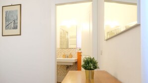 Een gang met een houten tafel en een potplant, een fotokader aan de muur en een badkamer die zichtbaar is door een geopende deur.