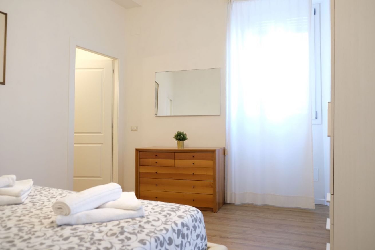 Une chambre à coucher avec un lit, une commode en bois, un miroir et une porte.