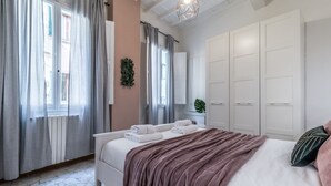 A bedroom with a bed, a bedside table, a wardrobe, and a window with curtains. - Wine Apartments Florence Sangiovese (Firenze)