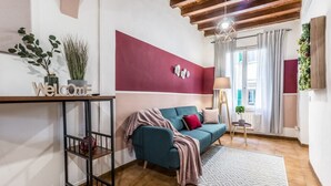 A modern living room with a teal sofa, a red accent wall, a wooden ceiling, and a small side table with a lamp. - Wine Apartments Florence Sangiovese (Firenze)