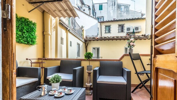 An outdoor seating area with wicker furniture, a table with a teapot and cups, and a potted plant. - Wine Apartments Florence Sangiovese (Firenze)