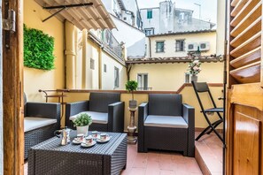 An outdoor seating area with wicker furniture, a table with a teapot and cups, and a potted plant. - Wine Apartments Florence Sangiovese (Firenze)