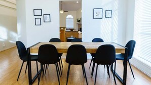 Un'area pranzo con tavolo in legno e sedie nere, quadri alle pareti e vista sulla cucina attraverso un arco.