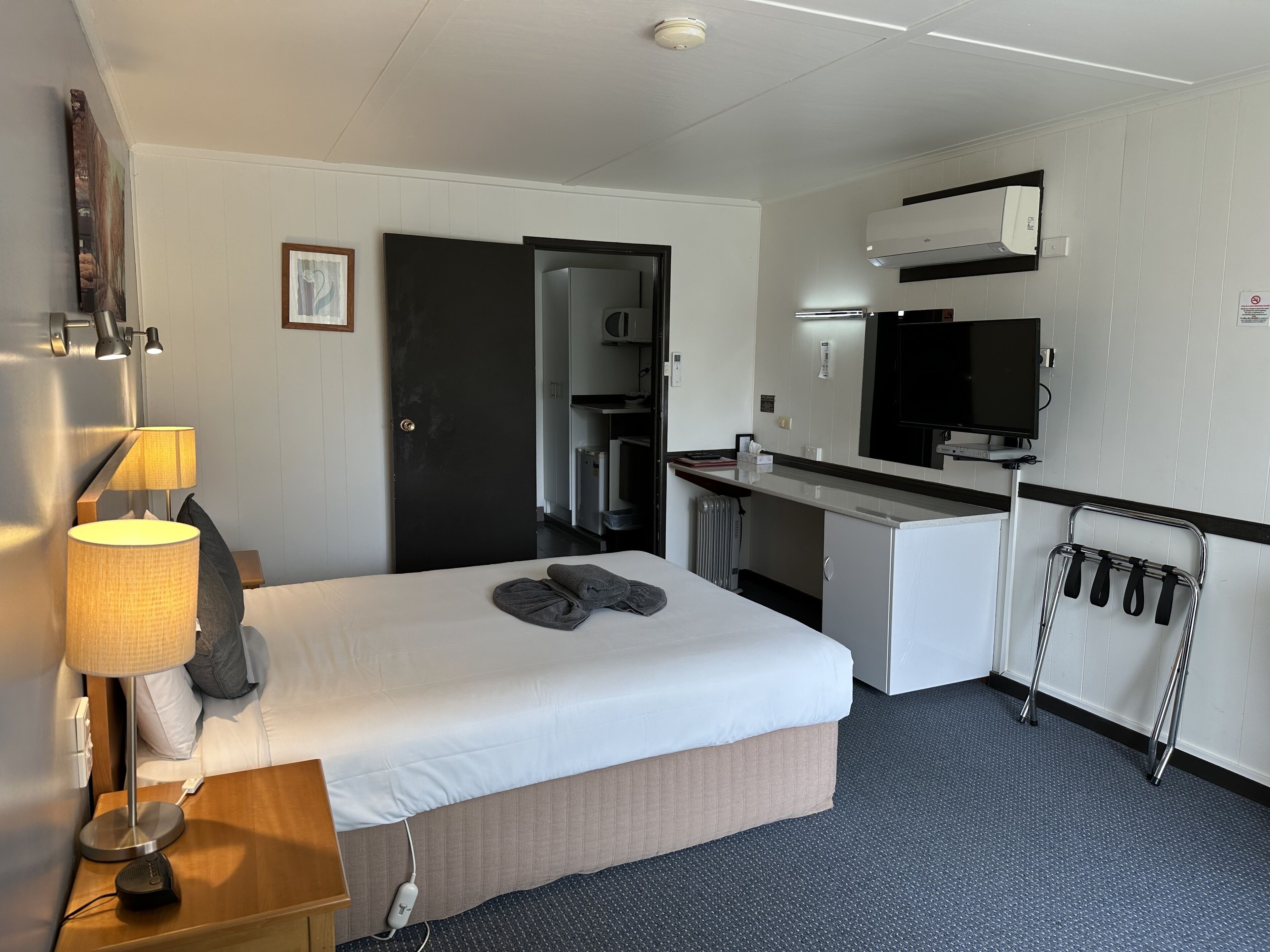 A hotel room with a bed, bedside lamp, desk, and a mirror.