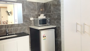 A compact kitchen with a microwave on a small fridge, white cabinets, a black countertop, and a tiled backsplash.