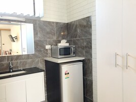 Una cocina compacta con microondas sobre un refrigerador pequeño, gabinetes blancos, una encimera negra y un rebozo de azulejos.