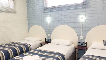 A hotel room with two single beds, each with a striped bedspread and white pillows. There are two bedside tables with lamps, and the walls are covered with blue brick-pattern wallpaper.