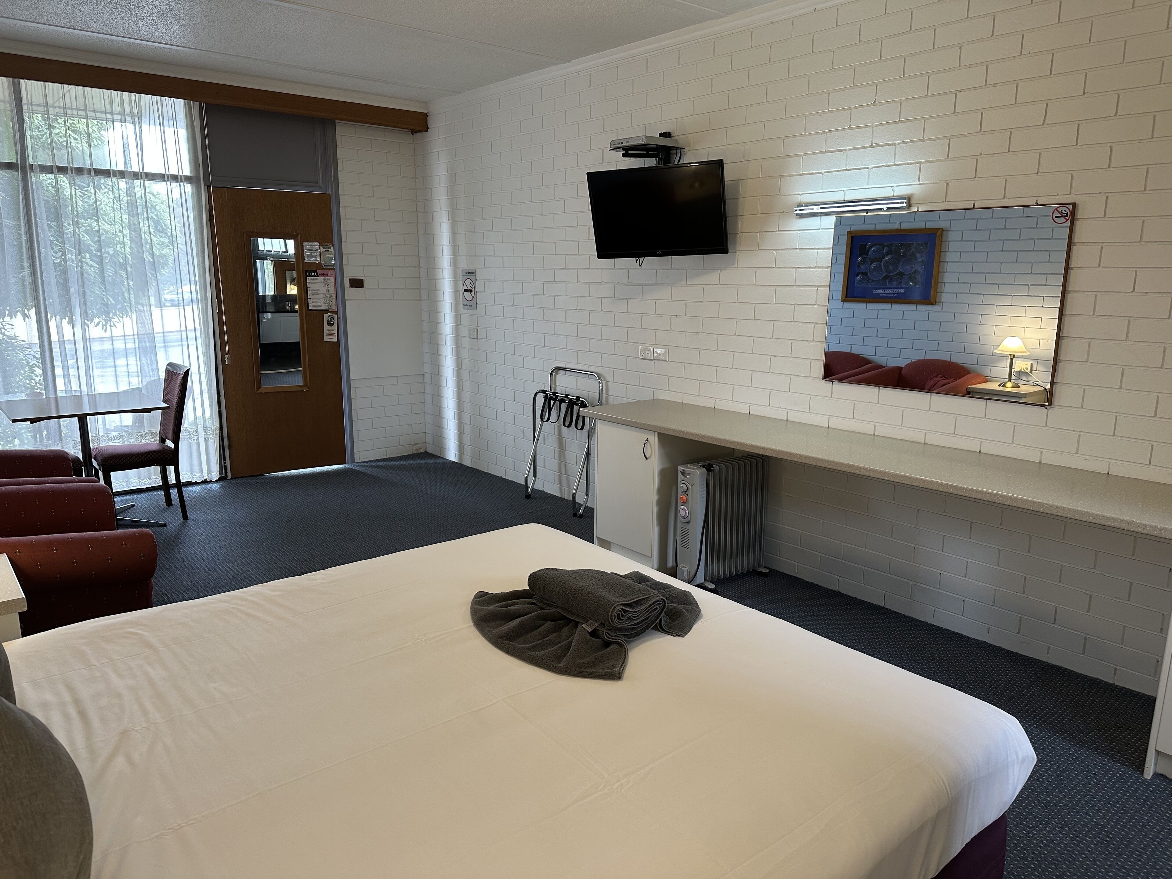 A hotel room with a bed, a desk, a chair, a TV, and a window with curtains.