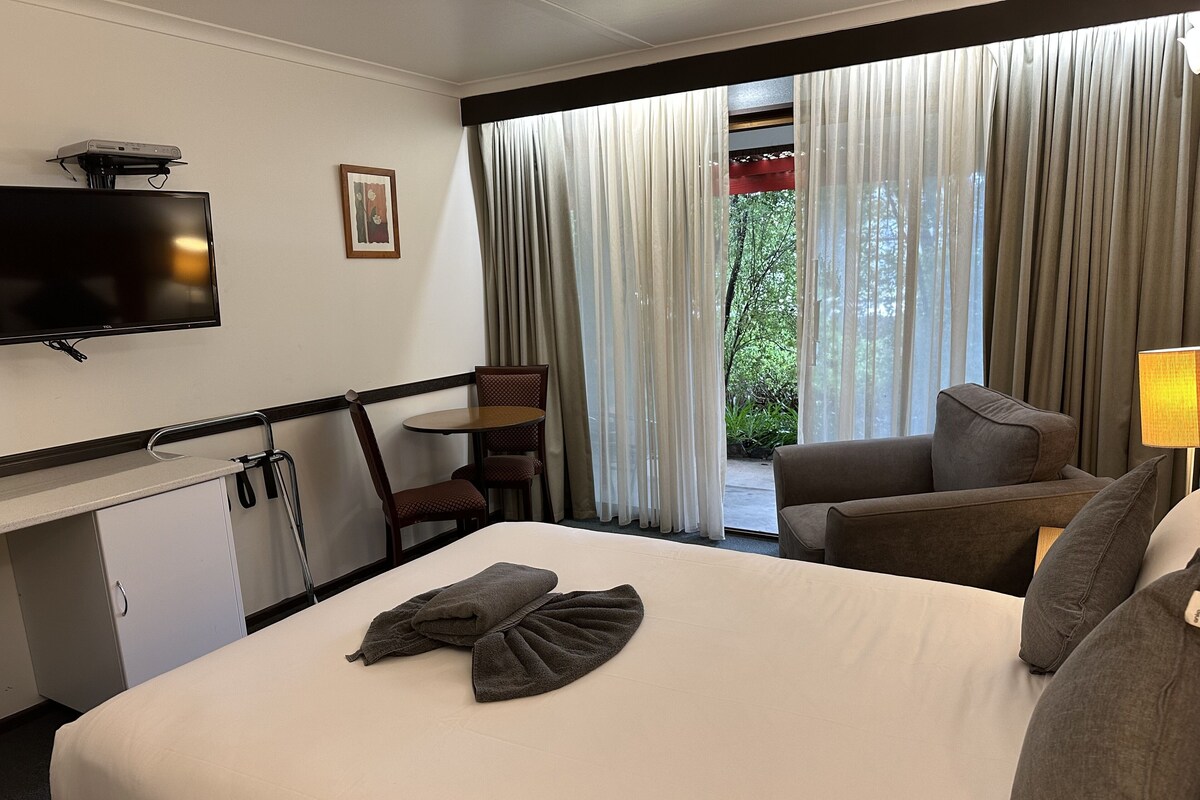 Ein Hotelzimmer mit einem Bett, einem Schreibtisch mit Fernseher, einem Sessel, einer Couch und einem Fenster mit Vorhängen.