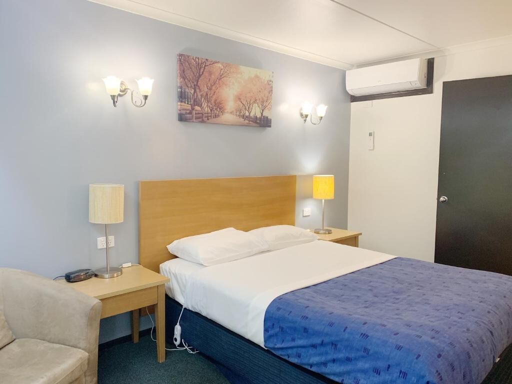 Una habitación de hotel con cama, lámparas de noche, un cuadro en la pared y un equipo de aire acondicionado.