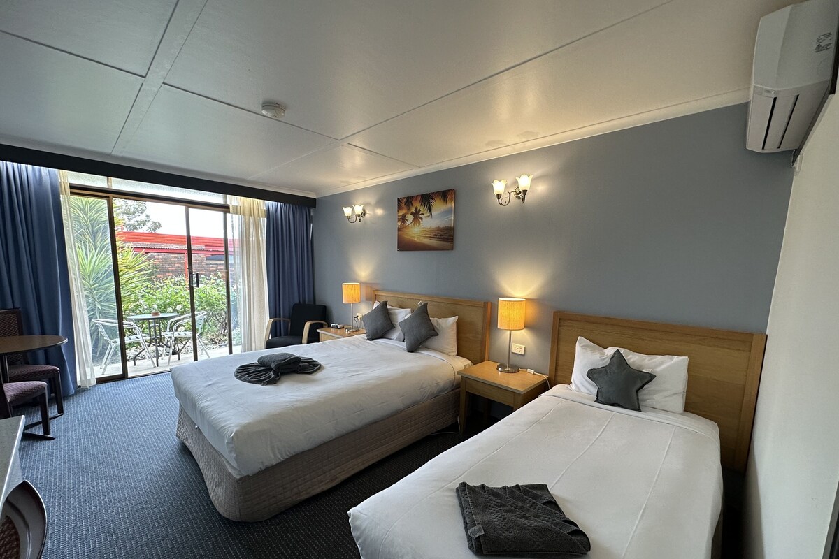 Ein Hotelzimmer mit zwei Betten, einem Schreibtisch, einem Stuhl, einem Tisch und Blick ins Freie.