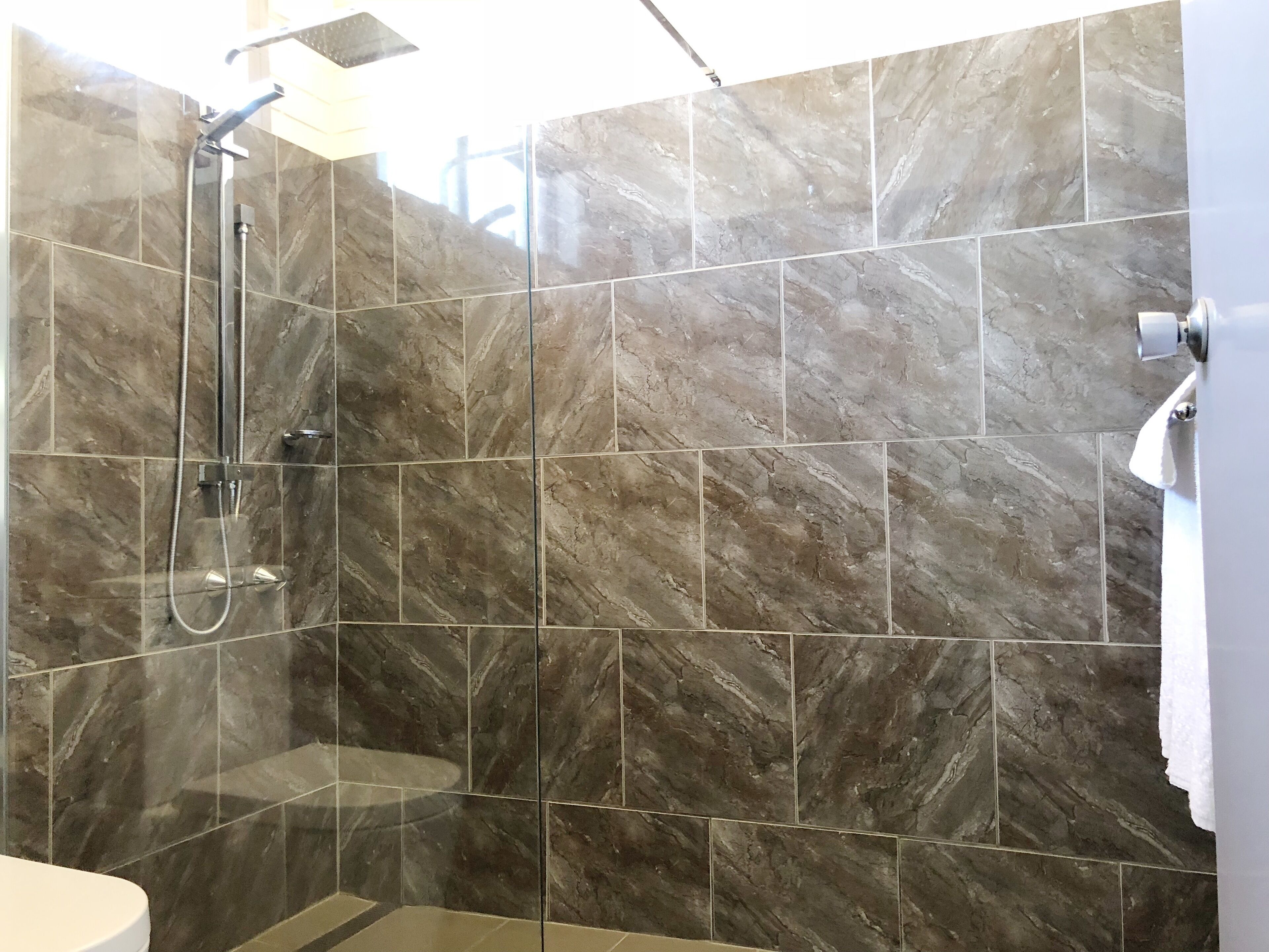 A modern bathroom with a shower area, marble tiles, and a toilet.