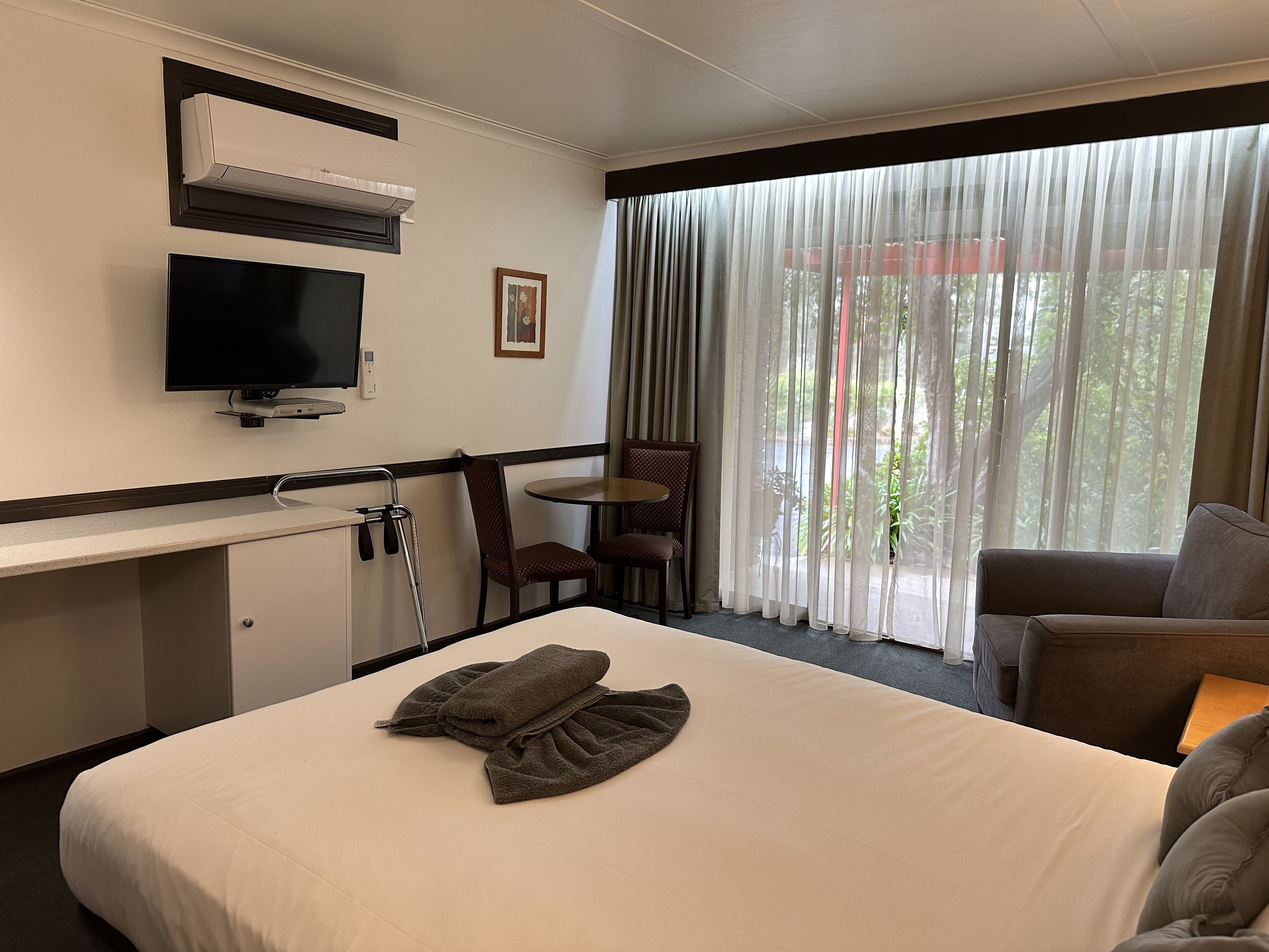 A hotel room with a bed, a TV, a desk, a chair, and a window with curtains.
