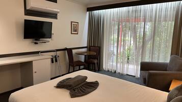 Una camera d'albergo con un letto, una TV, una scrivania, una sedia e una finestra con tende.