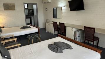 Una habitación de hotel con dos camas individuales, una kitchenette pequeña, un televisor montado en la pared y un espejo sobre el lavamanos.