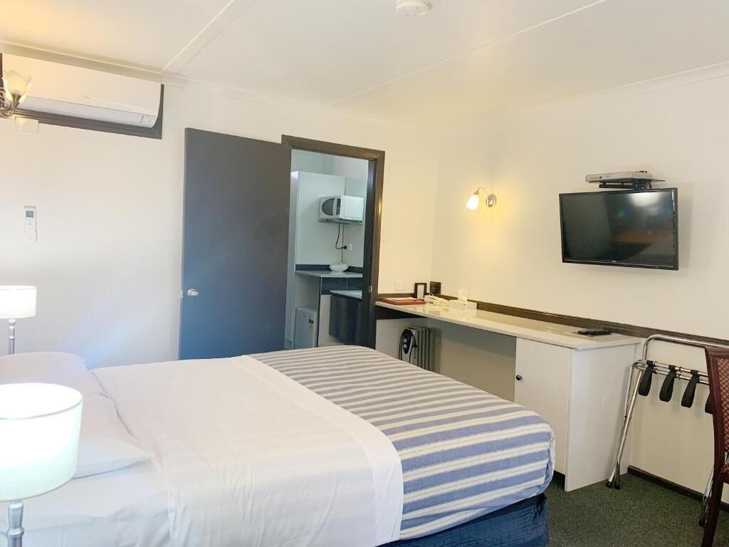 Habitación de hotel con cama, escritorio, televisor, microondas y una silla con bandeja.