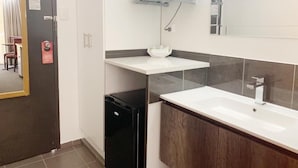 A modern bathroom with a white sink, a mirror, and a microwave above the countertop.