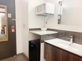 Un baño moderno con un lavamanos blanco, un espejo y un microondas sobre la encimera.