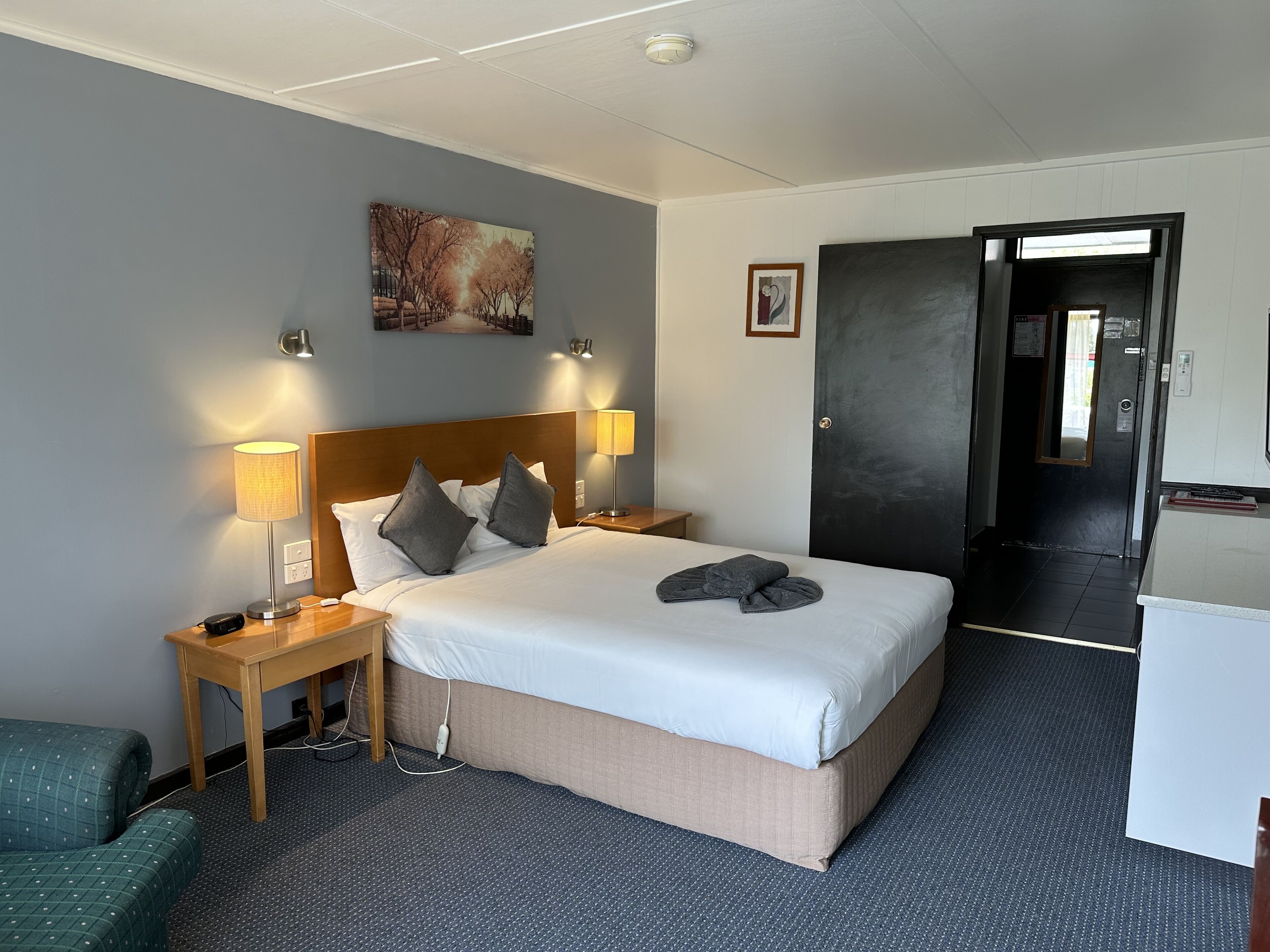 A hotel room with a large bed, two bedside lamps, a painting on the wall, and a door leading to a hallway.