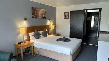 A hotel room with a large bed, two bedside lamps, a painting on the wall, and a door leading to a hallway.