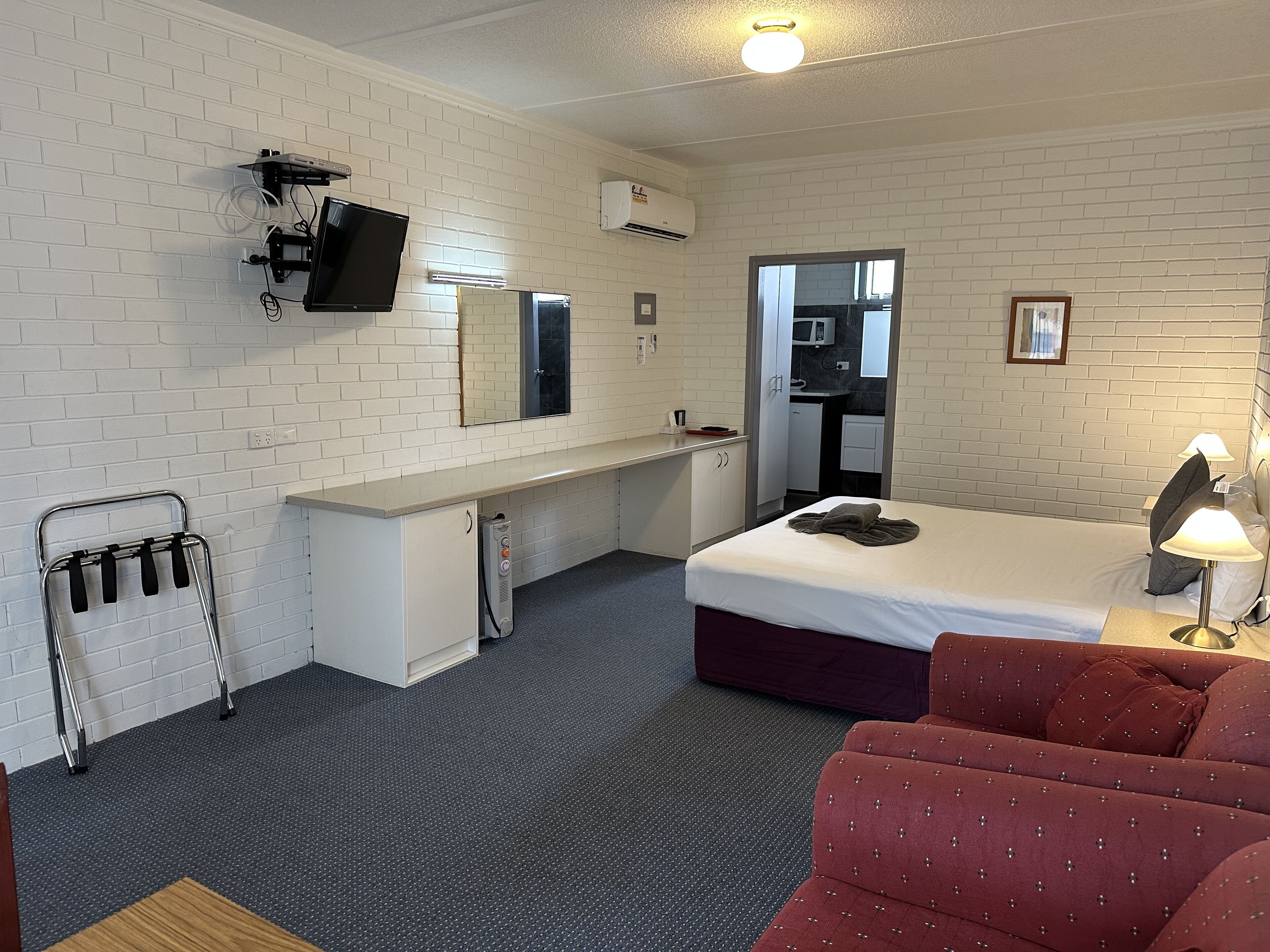 Habitación de hotel con cama, escritorio, silla, televisor y microondas en una esquina.