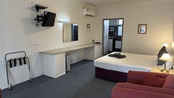 Habitación de hotel con cama, escritorio, silla, televisor y microondas en una esquina.