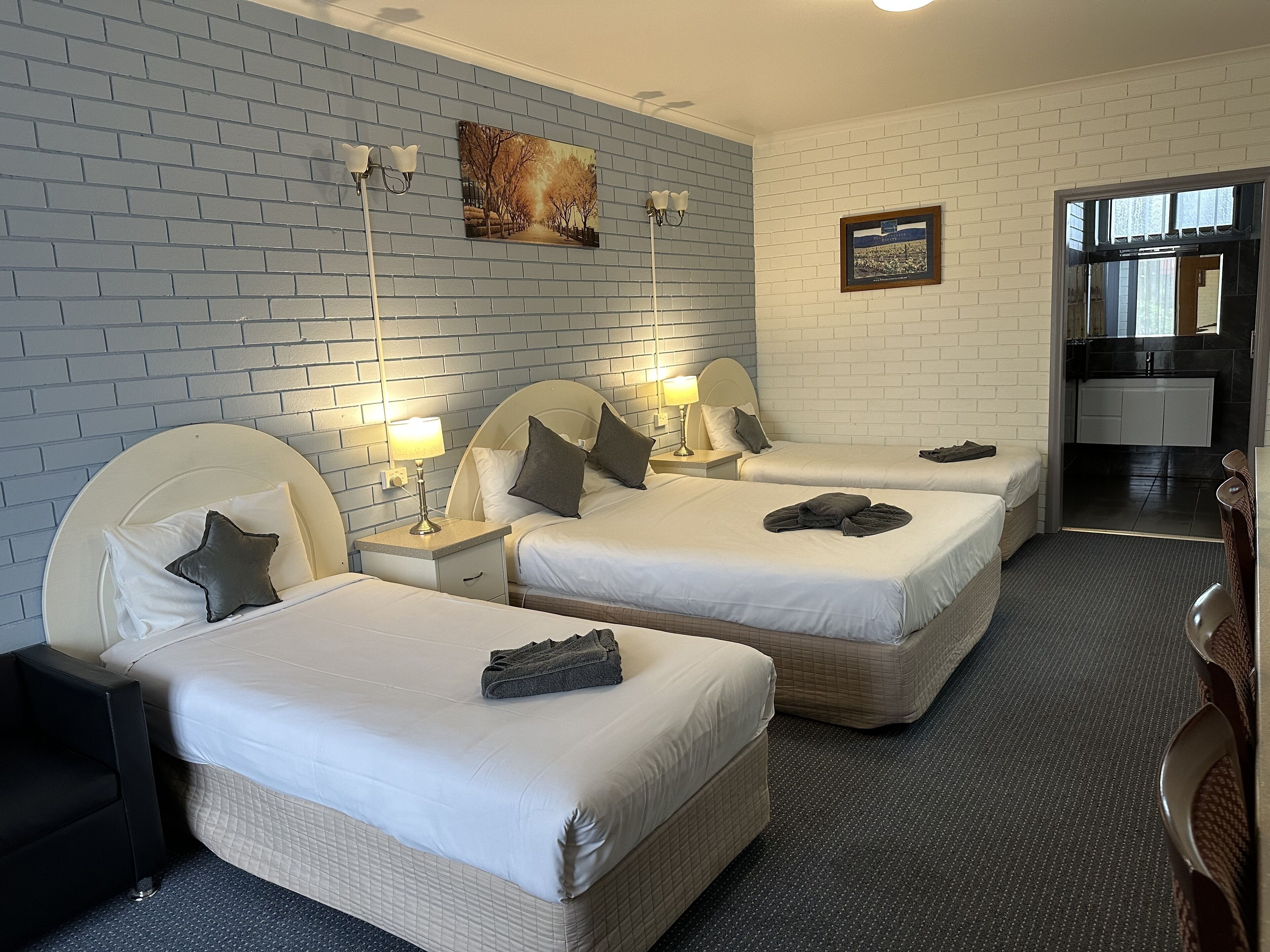 A hotel room with two beds, a small kitchenette, and a bathroom.
