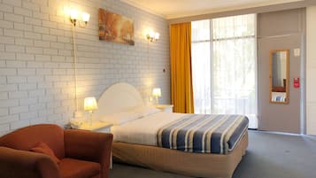 A hotel room with a white brick wall, a bed with striped bedding, a red armchair, and a large window with yellow curtains.