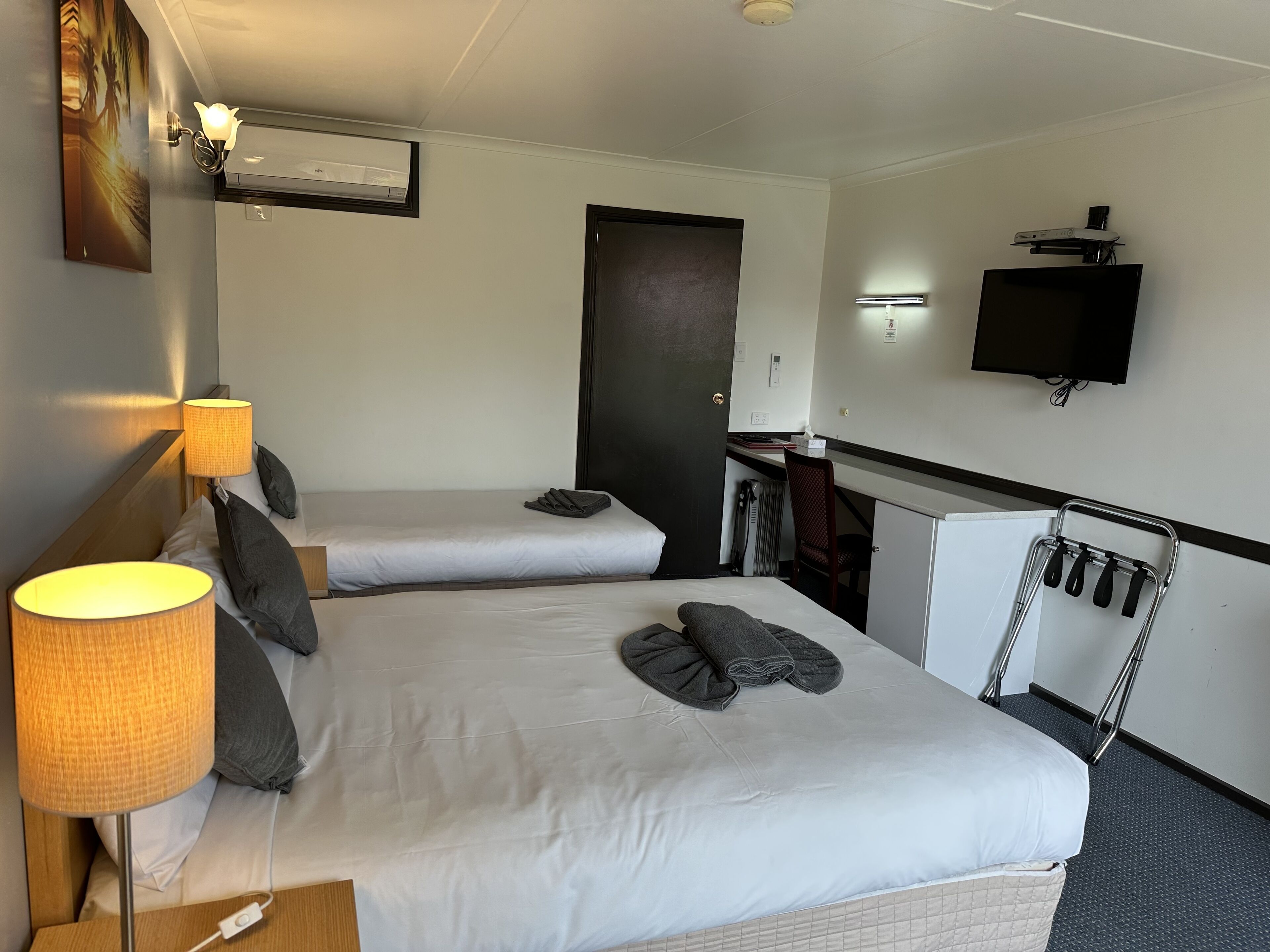 Ein Hotelzimmer mit zwei Betten, einem Schreibtisch, einem Fernseher und einem Kleiderständer.