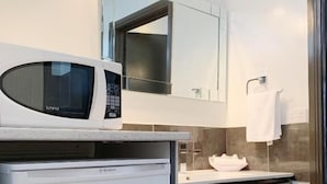 A compact bathroom with a microwave on a countertop, a sink with a white basin, and a mirror above the sink.