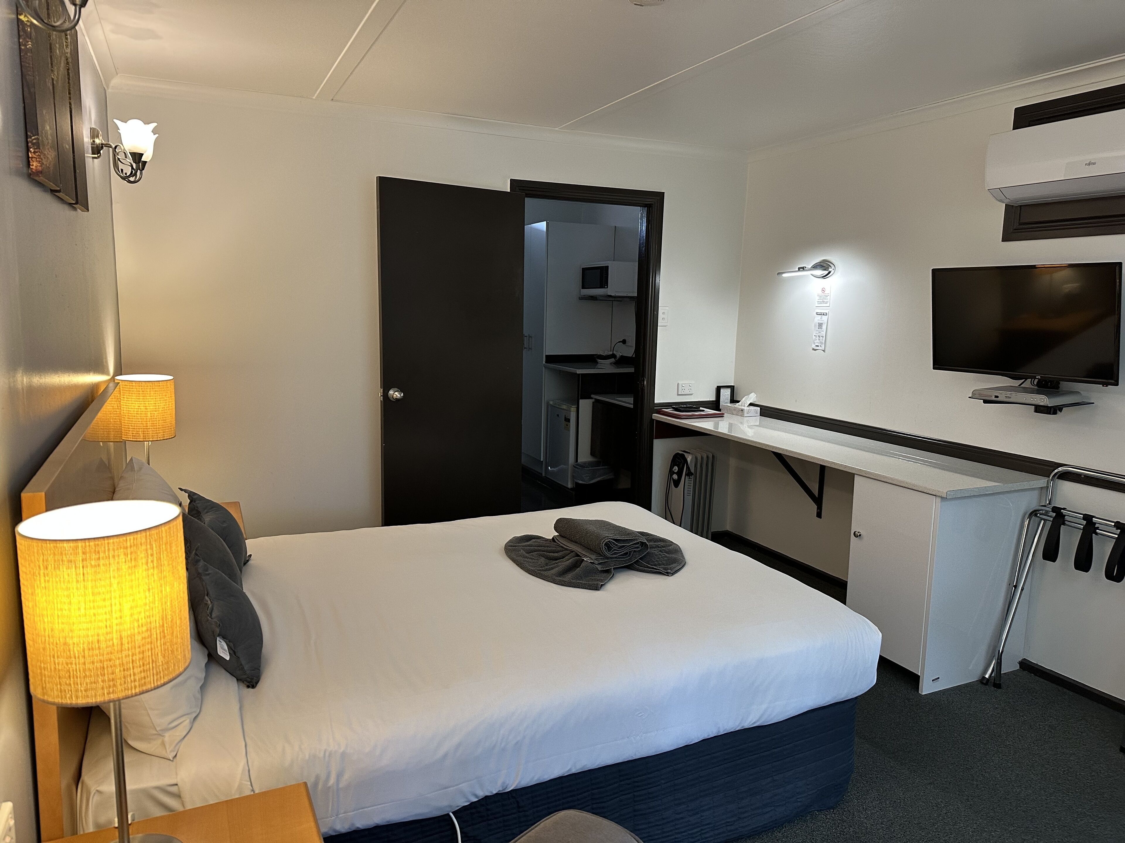 Ein Hotelzimmer mit Bett, Schreibtisch, Fernseher, Lampe und einer Tür.