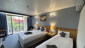 A hotel room with two beds, a desk, a chair, a table, and a view of the outdoors.